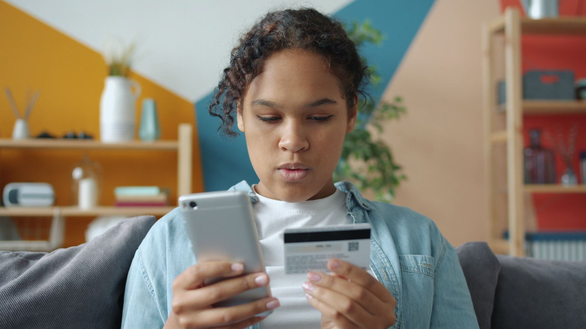 A young woman on her sofa holding her card and checking a charge on her phone