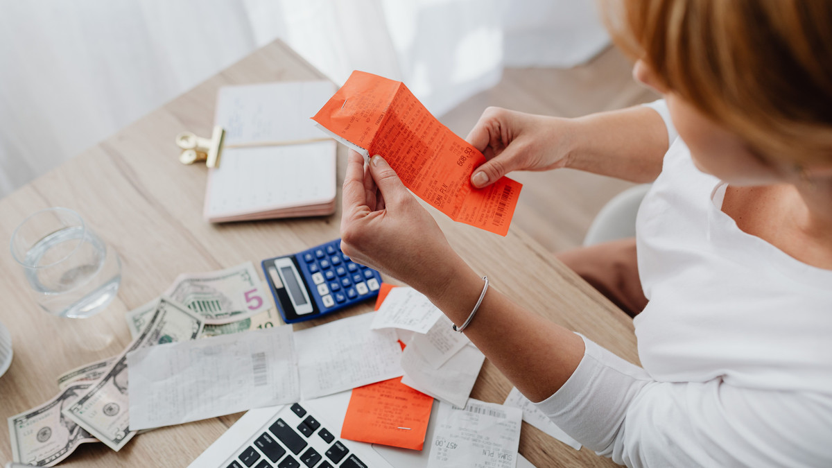 Person going through receipts and bills at a desk with a calculator and laptop