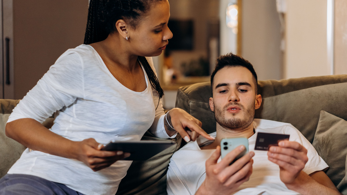 Couple on a sofa, one holding a payment card while checking a charge on his phone