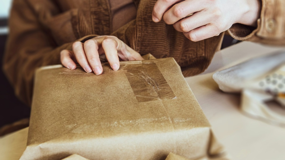 Hands unwrapping a subscription delivery in brown kraft paper