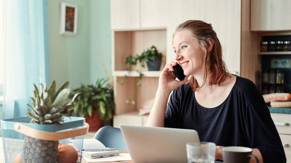 Smiling customer on a phone call at her kitchen table, with a laptop open in front of her
