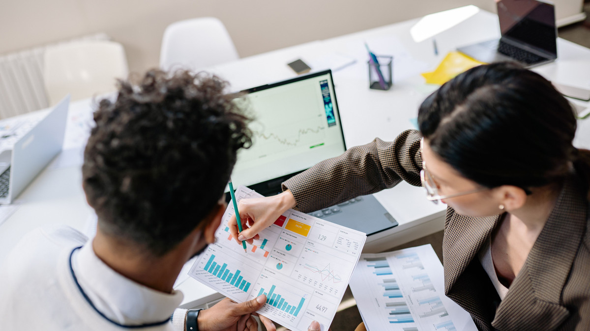 Two colleagues reviewing printed charts and a laptop dashboard at a meeting table