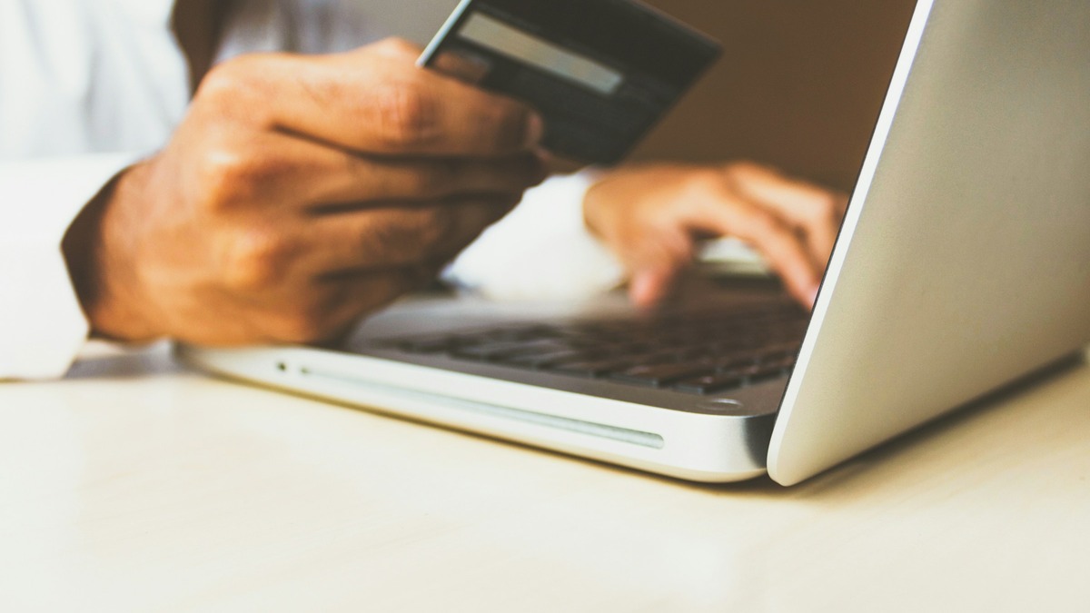 Hand holding a payment card while shopping online on a laptop